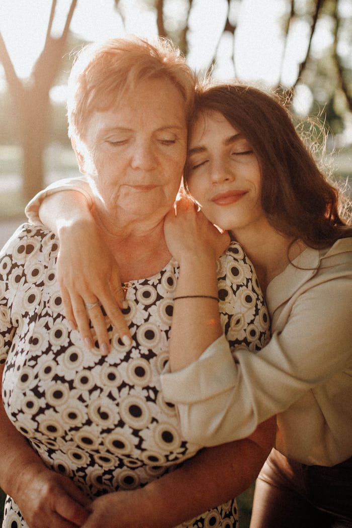 A heartwarming moment capturing a mother and daughter embracing outdoors in sunlight.