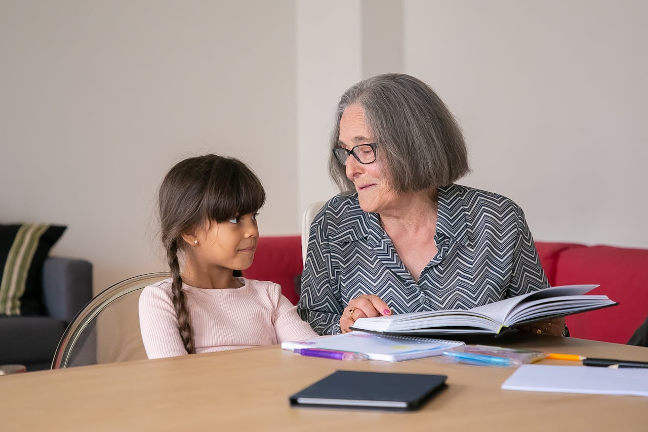 An elderly woman and a young girl sharing a book indoors, fostering a bond through reading.